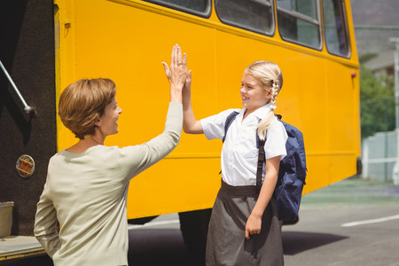 Mother with her daughter by school bus outside the elementary schoolの写真素材