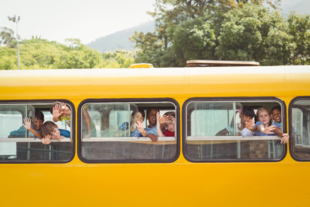 Cute pupils smiling at camera in the school bus outside the elementary schoolの写真素材