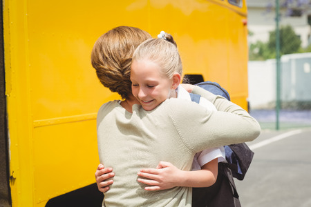 Mother hugging her daughter by school bus outside the elementary schoolの写真素材