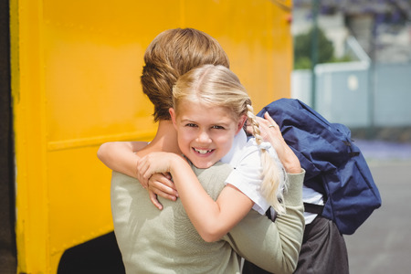 Mother hugging her daughter by school bus outside the elementary school