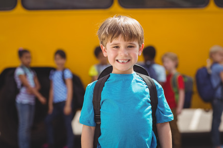 Cute pupils smiling at camera by the school bus outside the elementary schoolの写真素材