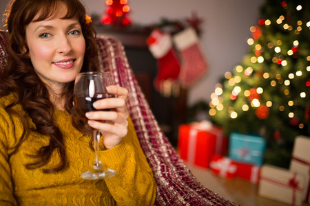 Woman sitting on a couch while holding a glass of red wine at christmas at home in the living roomの写真素材