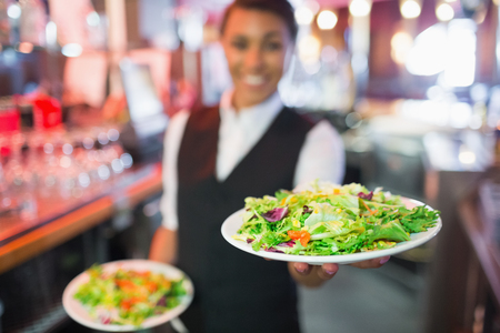Pretty barmaid holding plates of salads in a barの写真素材