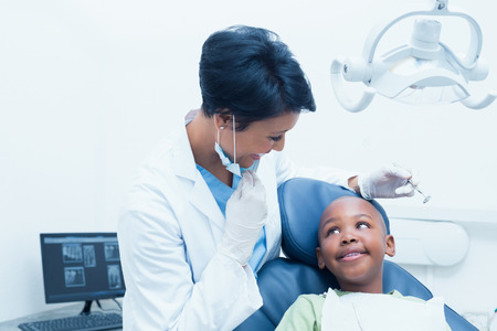 Portrait of smiling female dentist examining boys teeth in the dentists chairの写真素材