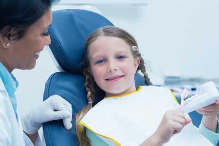 Female dentist teaching girl how to brush teeth in the dentists chairの写真素材