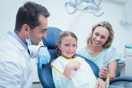 Dentist examining girls teeth in the dentists chair with assistantの写真素材