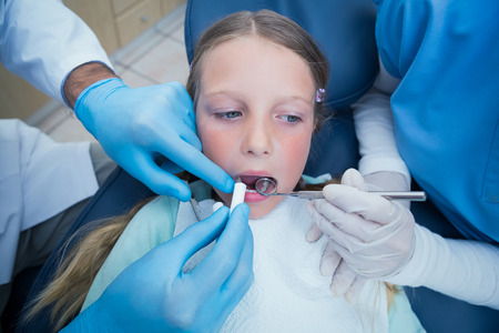 Dentist with assistant examining girls teeth in the dentists chairの写真素材