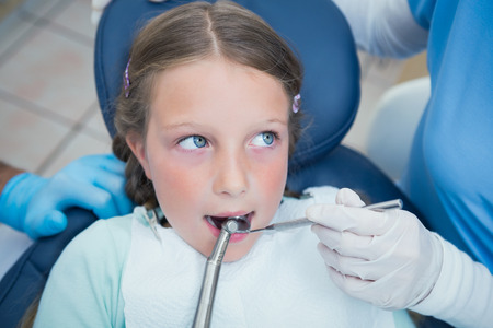 Dentist with assistant examining girls teeth in the dentists chairの写真素材