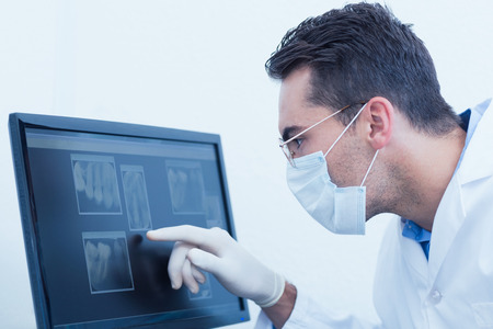 Concentrated male dentist looking at x-ray on computerの写真素材