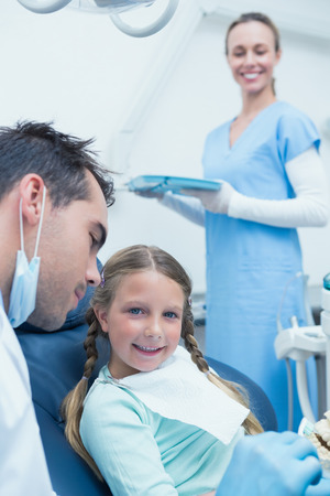 Male dentist teaching girl how to brush teeth in the dentists chairの写真素材