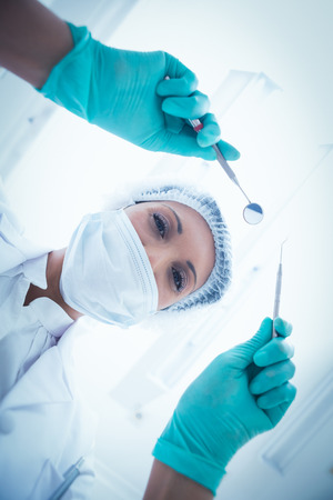 Portrait of female dentist in surgical mask holding dental toolsの写真素材