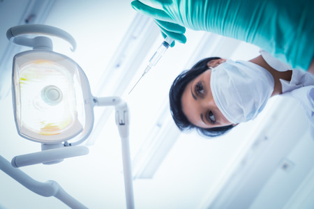 Low angle view of female dentist in surgical mask holding injectionの写真素材