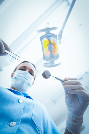 Low angle portrait of female dentist in surgical mask holding dental toolsの写真素材
