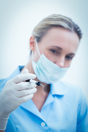 Portrait of young female dentist in surgical mask holding injectionの写真素材