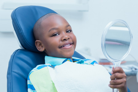 Smiling young boy holding at mirror in the dentists chairの写真素材