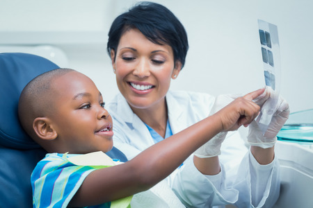 Female dentist showing young boy his mouth x-ray in the dentists chairの写真素材