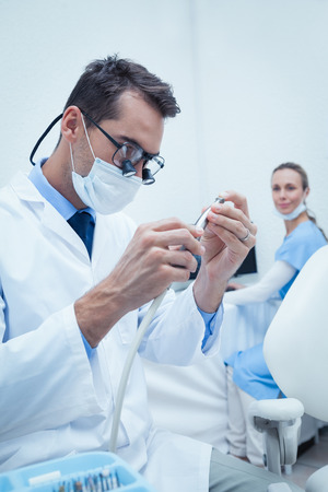 Concentrated young male dentist looking at dental toolの写真素材