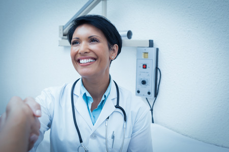 Cheerful female dentist shaking hands with cropped patientの写真素材