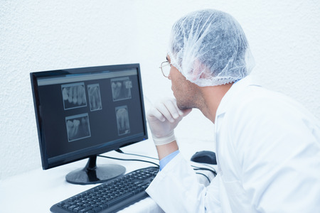 Concentrated male dentist looking at x-ray on computerの写真素材