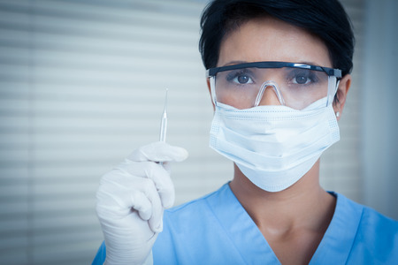 Portrait of female dentist in surgical mask holding dental toolの写真素材