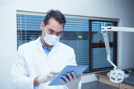 Concentrated male dentist in surgical mask using digital tabletの写真素材