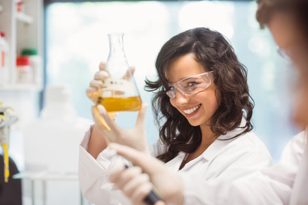 Pretty science student smiling and holding beaker at the university