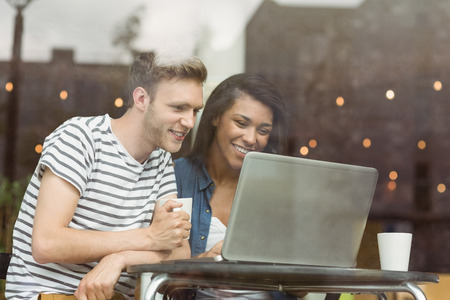 Smiling friends with a hot drink using laptop in cafe at the universityの写真素材