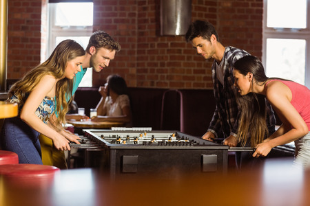 Smiling friends playing table football in a pub