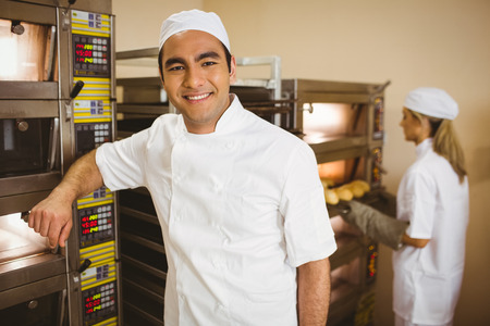 Handsome baker smiling at camera in a commercial kitchenの写真素材