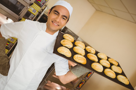 Baker smiling at camera holding tray of rolls in a commercial kitchen