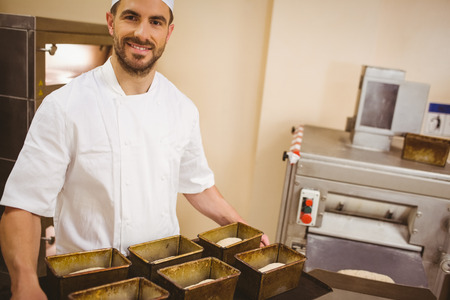 Happy baker holding tray of loaf tins in a commercial kitchen