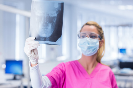 Dentist in mask and protective glasses holding an x-ray at the dental clinicの写真素材