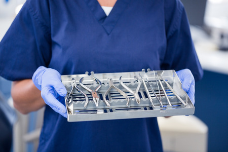 Dentist in blue scrubs holding tray of tools at the dental clinicの写真素材