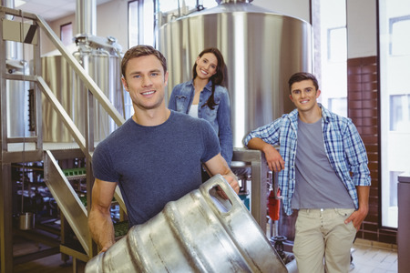 Young man holding keg with these colleagues behind him in the factory