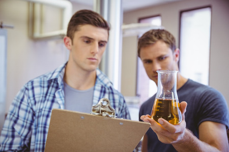 Two men looking at the beaker with beer in the factory