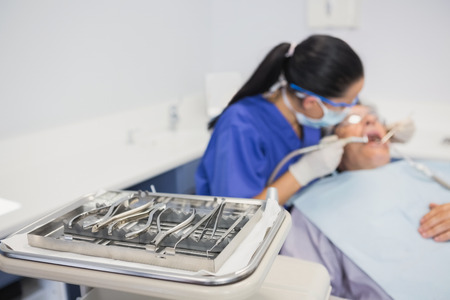 View of tray of dental equipment in front of a dentist with a patient