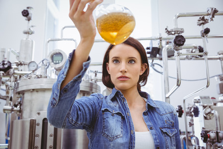 Stylish girl in denim jacket holding beaker of beer in the factoryの写真素材