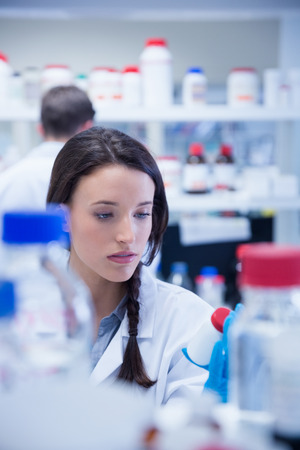 Young chemist picking up the bottles on the shelf in labの写真素材