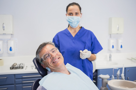 Dentist wearing surgical mask with a smiling patient in dental clinicの写真素材