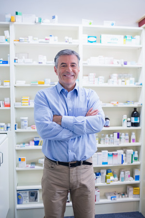 Portrait of a smiling pharmacist standing with arms crossed in the pharmacyの写真素材