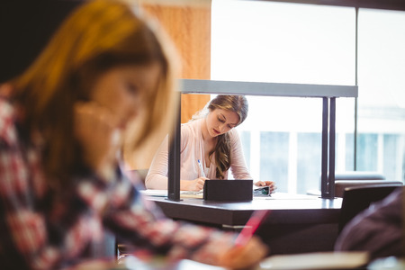 Focused student sitting next to the window taking notes in libraryの写真素材