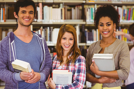 Students standing and smiling at camera holding books in libraryの写真素材