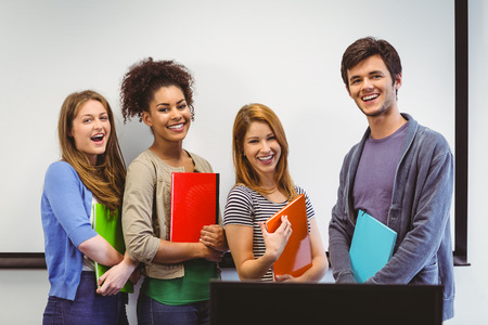 Students standing and smiling at camera holding notepads in classroomの写真素材