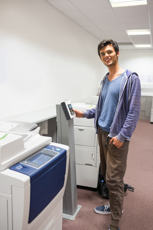 Smiling student standing next to the photocopier at the universityの写真素材