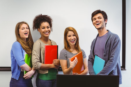 Students standing and smiling at camera holding notepads in classroomの写真素材