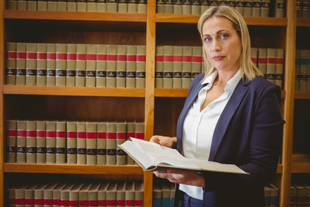 Woman reading concentrated a book standing in libraryの写真素材