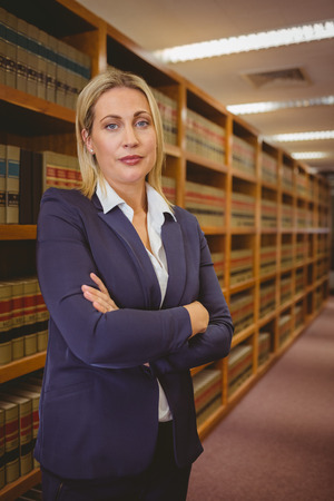 Serious woman standing with arms crossed in libraryの写真素材