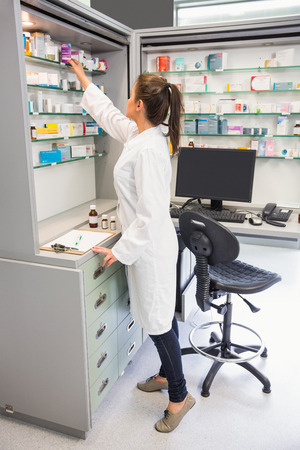 Junior pharmacist taking medicine from shelf at the hospital pharmacyの写真素材