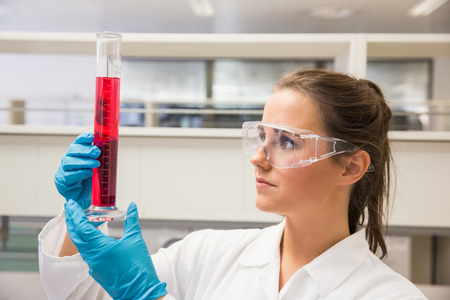 Young pharmacist holding beaker of red liquid at the laboratoryの写真素材