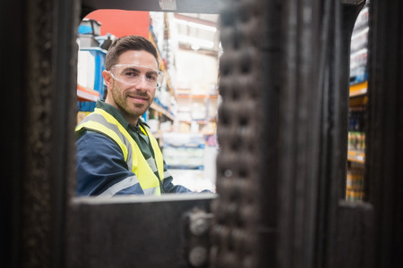 Smiling driver operating forklift machine in warehouse